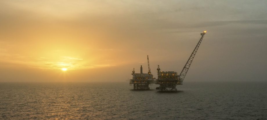 An oil rig in the middle of the ocean with the sun setting
